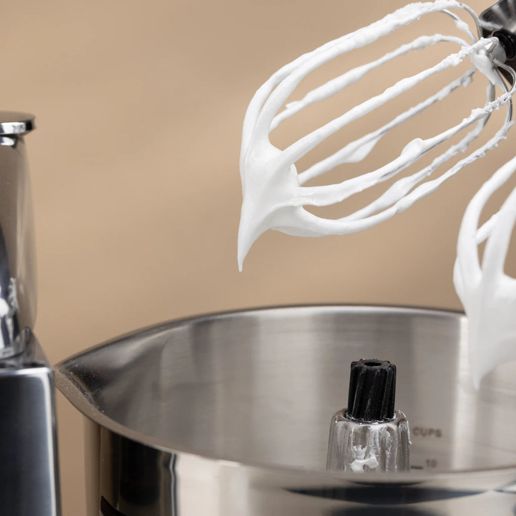 The Kitchen Table Ankarsrum stainless steel beater bowl with balloon whisks covered in fluffy whipped meringue.