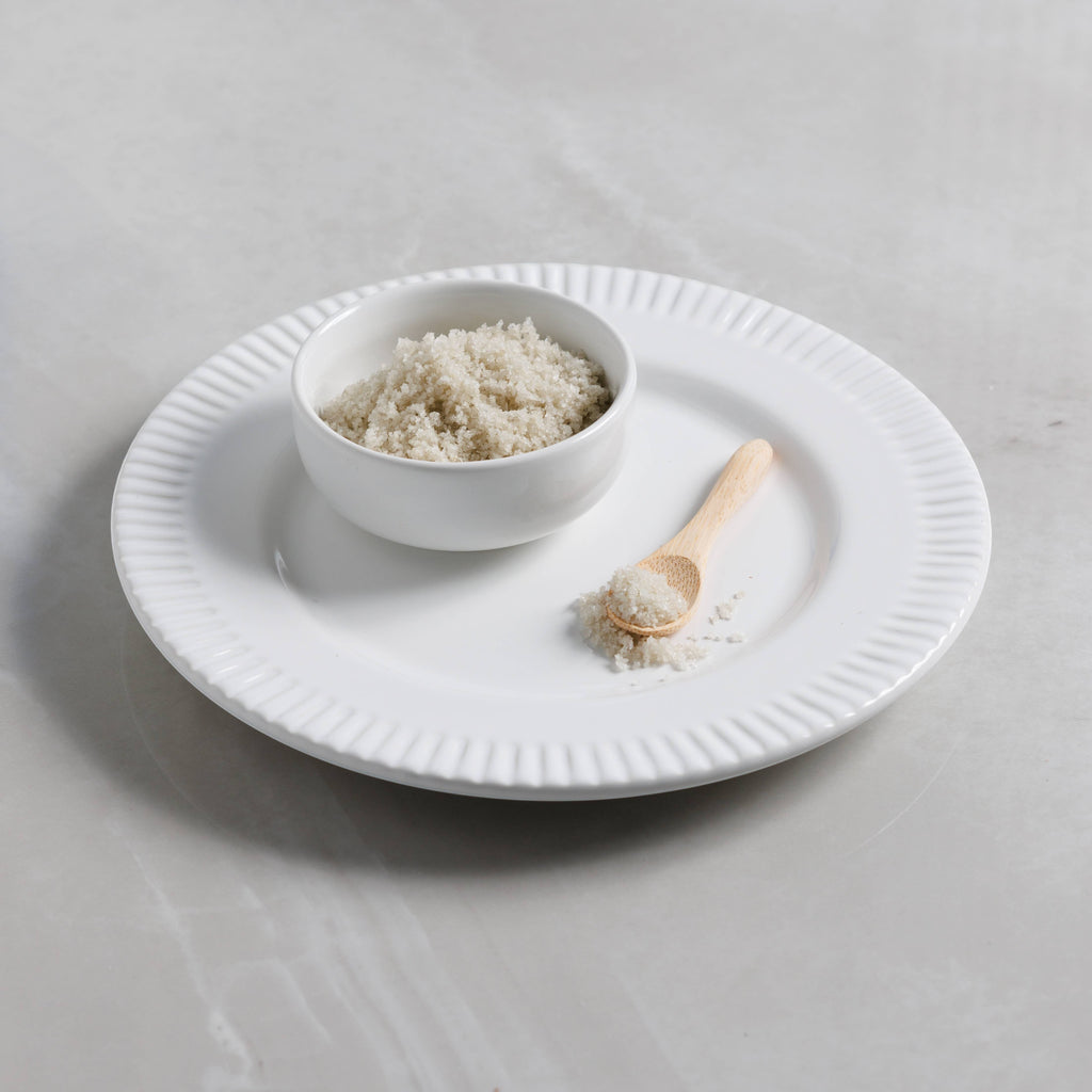 The Kitchen Table French Sel Gris grey sea salt in a small white bowl with a wooden spoon on a white plate