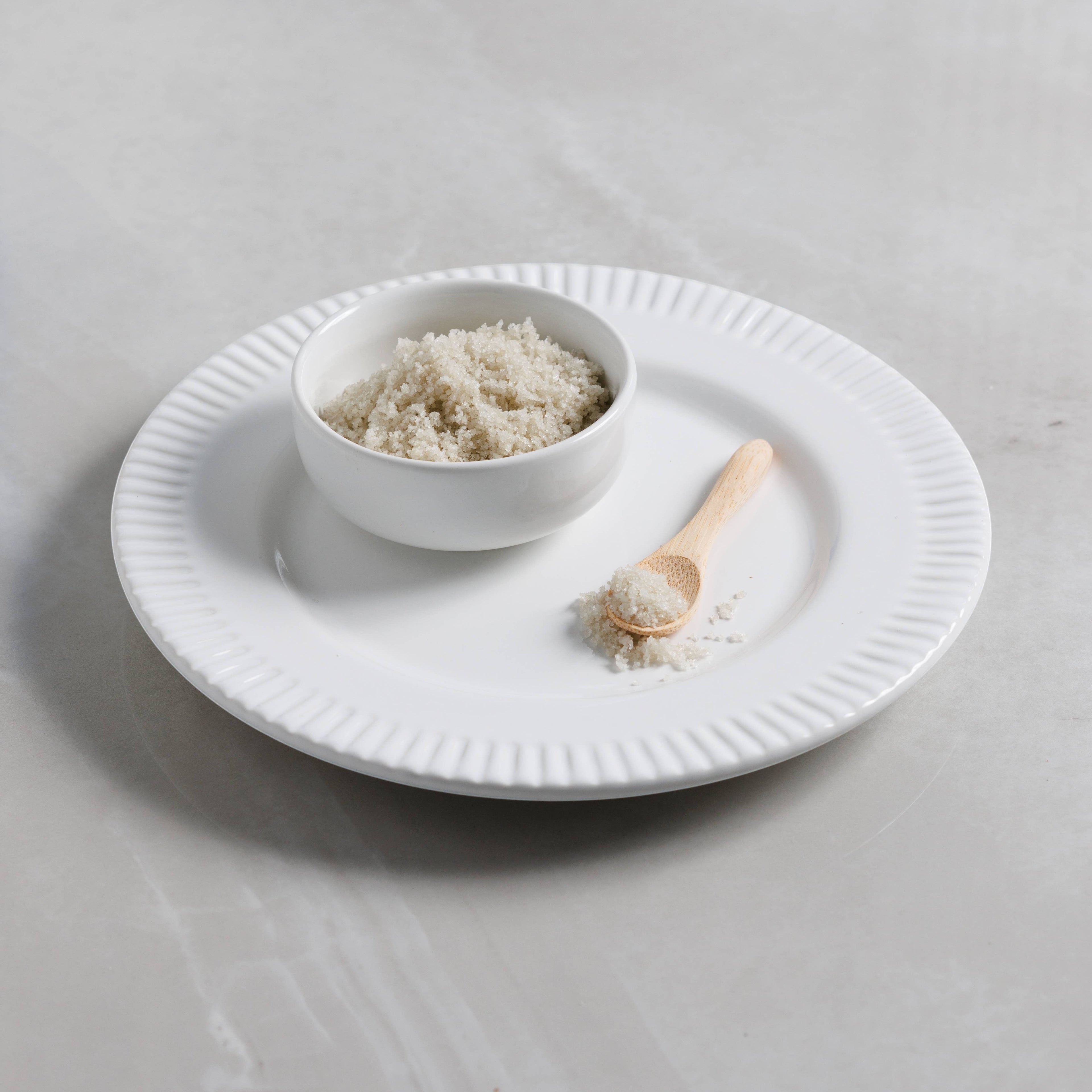 The Kitchen Table French Sel Gris grey sea salt in a small white bowl with a wooden spoon on a white plate