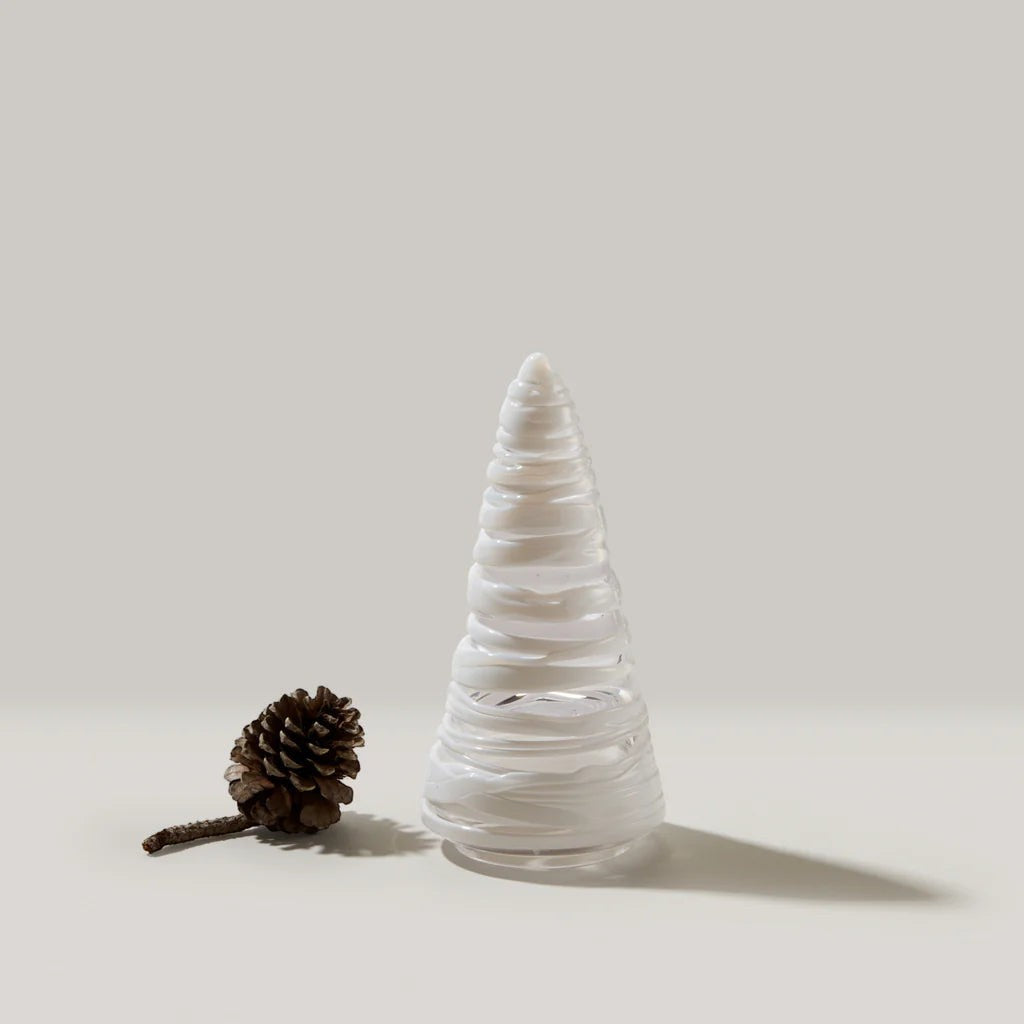 The Kitchen Table clear glass holiday tree ornament with white swirling details next to a small pinecone.