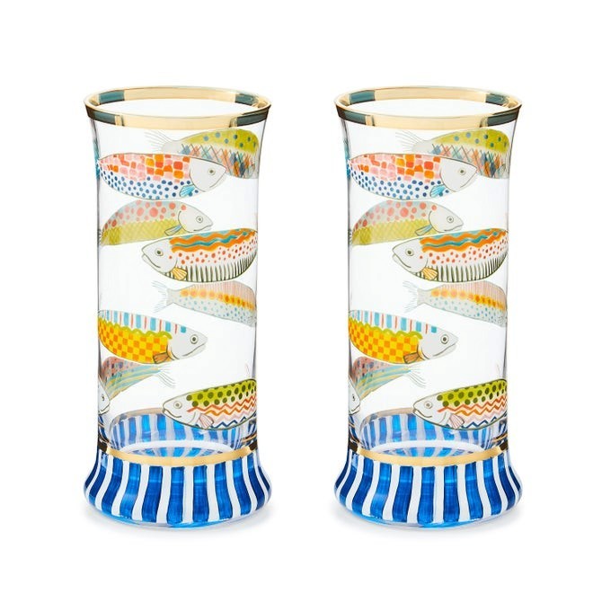 The Kitchen Table Go Fish highball glasses featuring colorful fish patterns, navy striped bases, and gold rim trim.