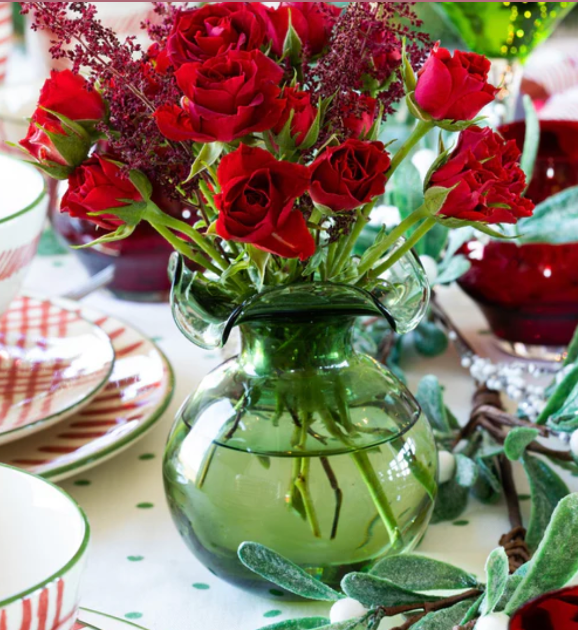 The Kitchen Table Hibiscus glass fluted bud vase in green holding a vibrant bouquet of red roses on a festive table.