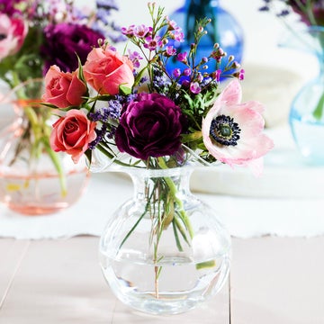 The Kitchen Table Hibiscus Glass fluted bud vase holding a vibrant bouquet of pink, purple, and white flowers.