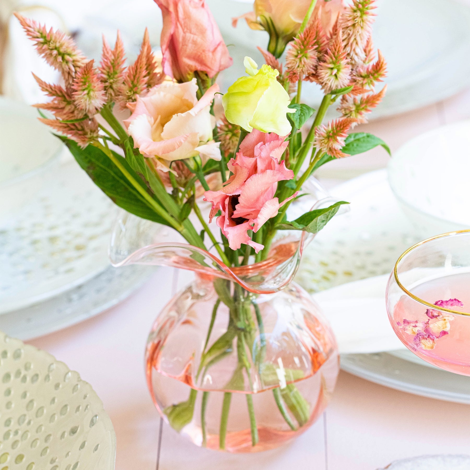 The Kitchen Table Hibiscus glass fluted bud vase in pink with a delicate floral arrangement on a dining table.