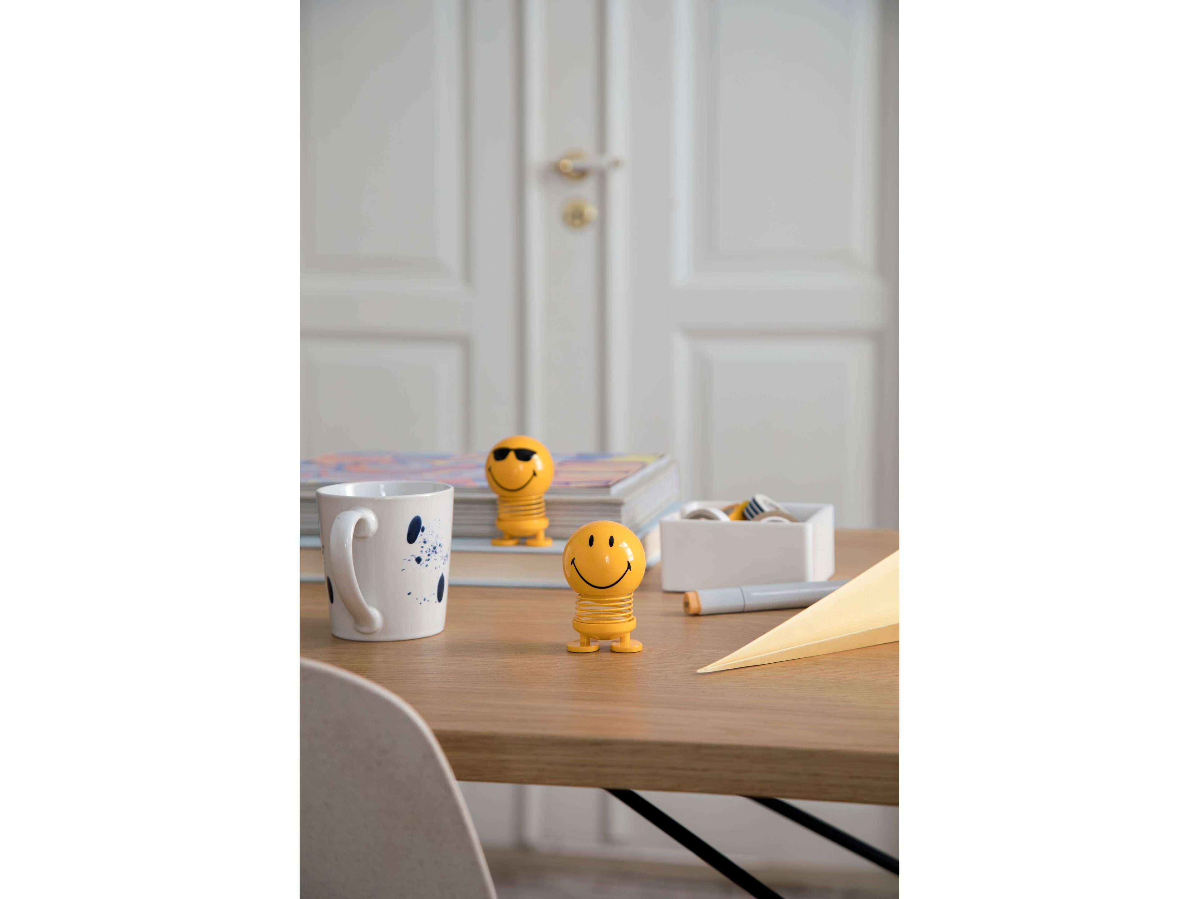 The Kitchen Table Hoptimist Smiley S yellow spring figurine with a beaming smile on a wooden desk