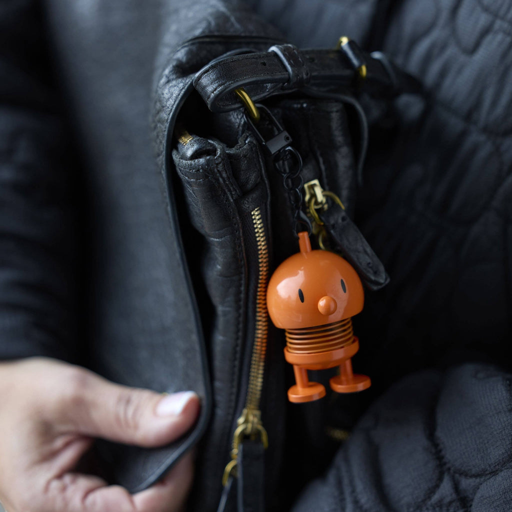The Kitchen Table orange Hoptimist bag charm clipped onto a black leather handbag zipper