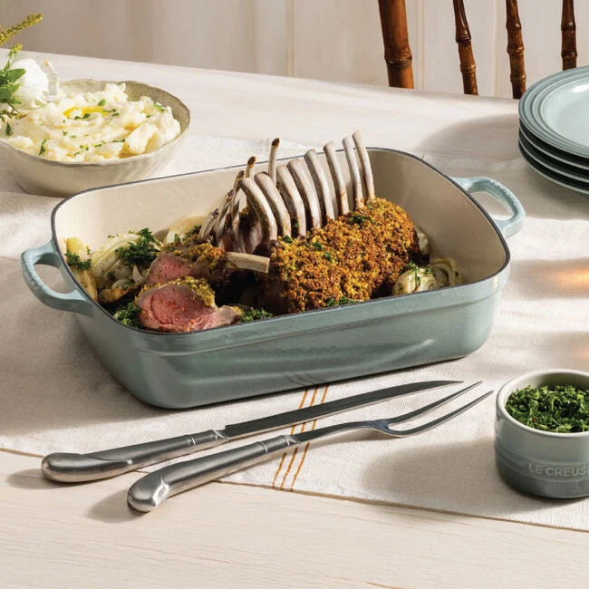 The Kitchen Table Le Creuset Signature rectangular enameled cast iron roaster filled with a roasted rack of lamb on a table