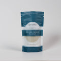 The Kitchen Table Sel Gris French sea salt in a teal stand-up pouch with a clear window showing grey mineral salt.