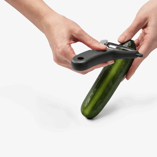 The Kitchen Table Dreamfarm Sharple Y-Peeler with ergonomic black handle peeling a fresh "Kermit green" cucumber