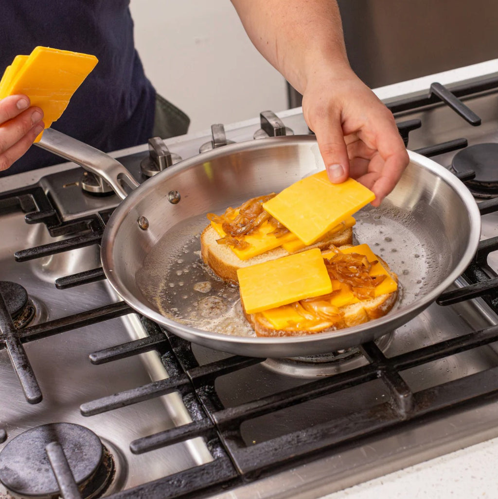 The Kitchen Table 12-inch stainless steel fry pan cooking grilled cheese sandwiches with melted cheddar on a stovetop