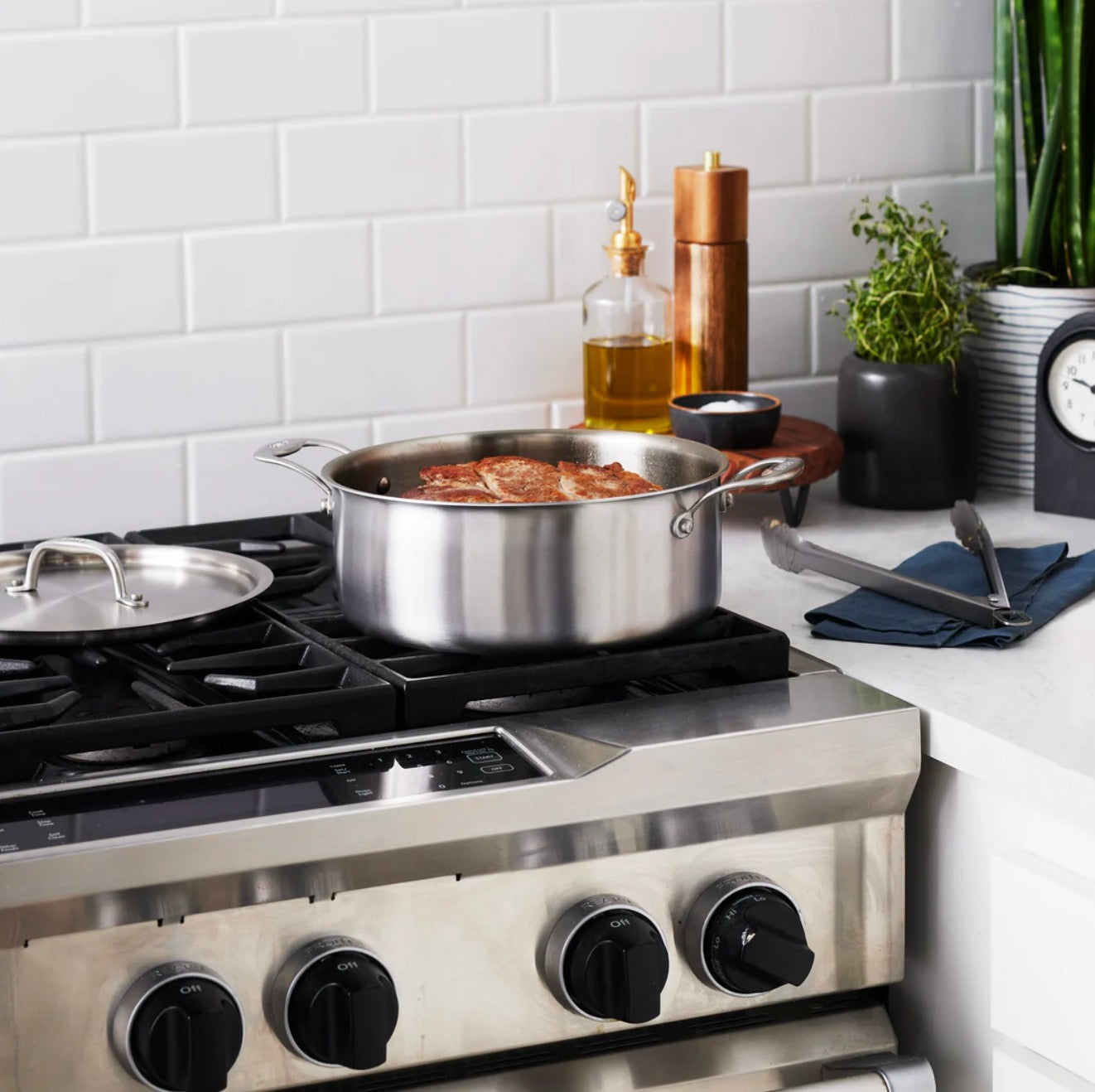 The Kitchen Table 6 quart stainless steel rondeau pan with lid on a gas stove, perfect for braising and searing.