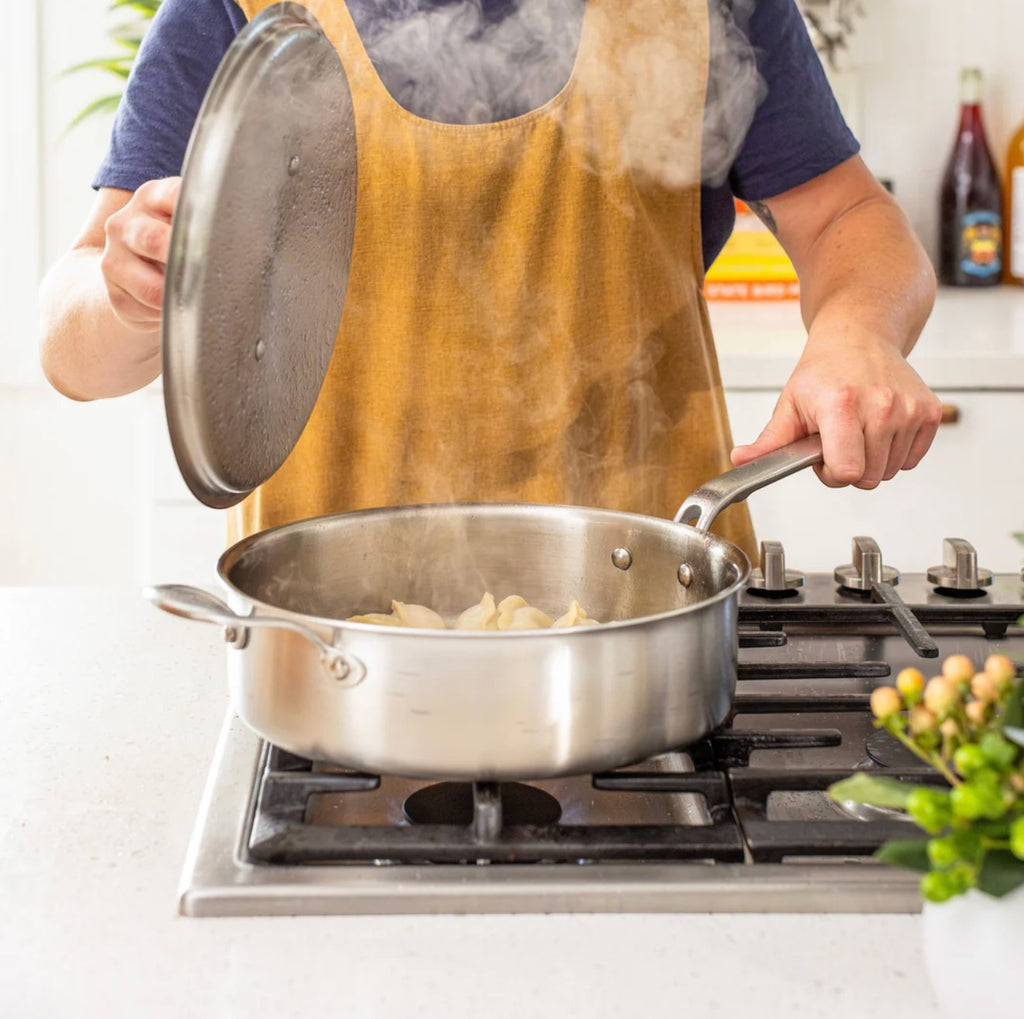 The Kitchen Table 4 quart stainless steel sauté pan with lid being used to cook food on a stovetop