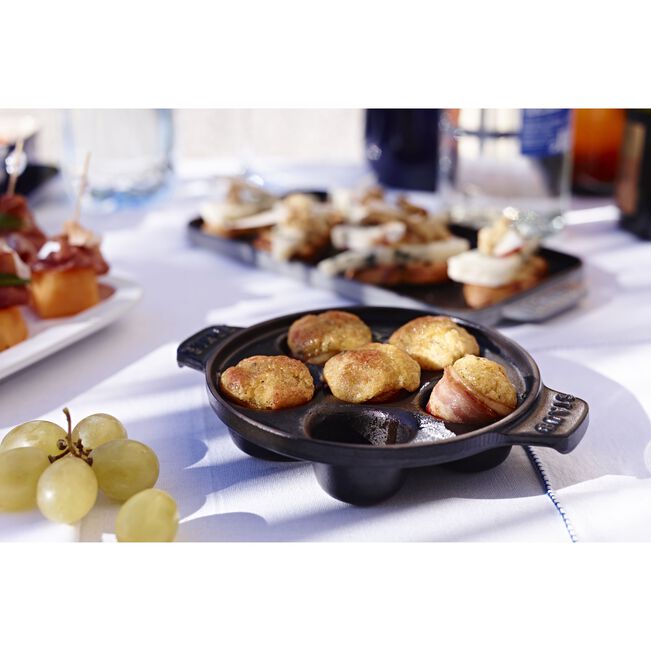 The Kitchen Table Staub cast iron escargot dish with six holes, filled with cooked appetizers on a dining table.