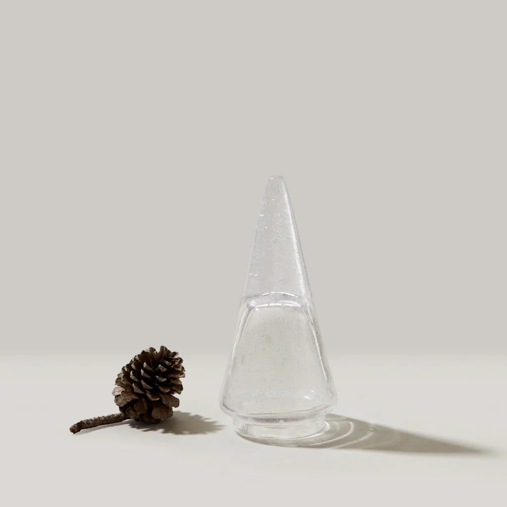 The Kitchen Table Vela Conical Evergreen glass tree ornament with internal bubbles next to a small pinecone.